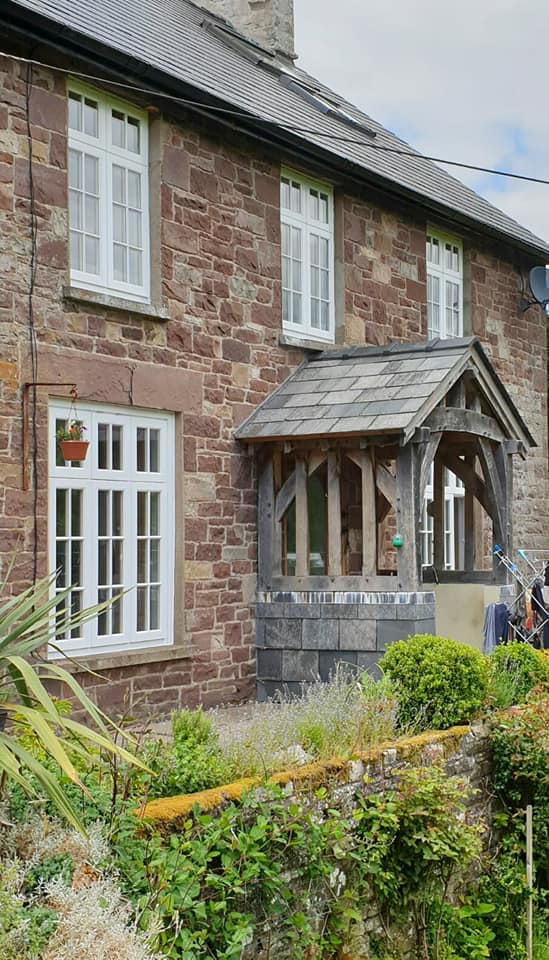 White-painted casement windows and a green-oak porch on a red-sandstone Powys cottage, made by Crickhowell Joinery